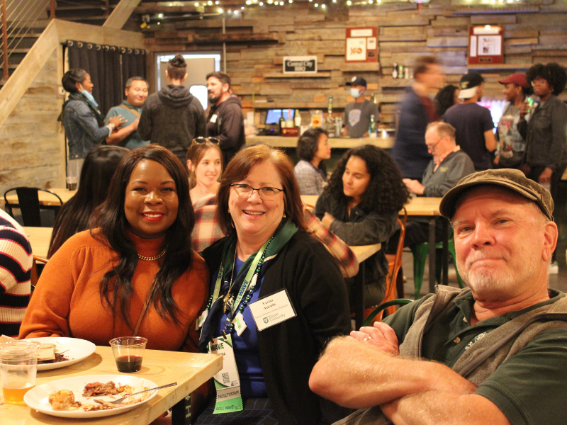 Alumna poses with woman and professor while seated at a table at the alumni reception