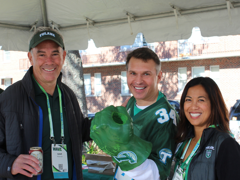 Professor poses with others dressed in Tulane swag at tailgate