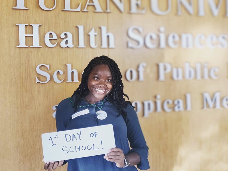 Student holding a handwritten sign that reads "first day of grad school!"