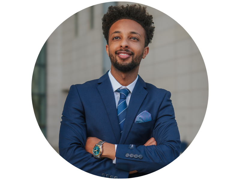 Caleb Hailemariam headshot, standing with arms crossed, wearing a suit, looking into distance. 