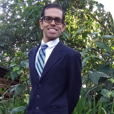 Aaron Koenig wearing a suit, smiling at camera, lush green plants in background