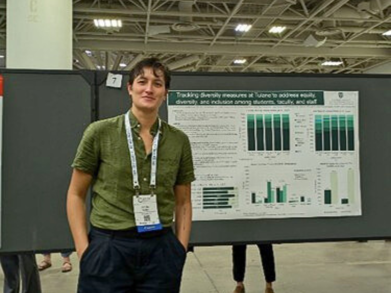 Smiling person stands by a scientific research poster in a large conference hall.