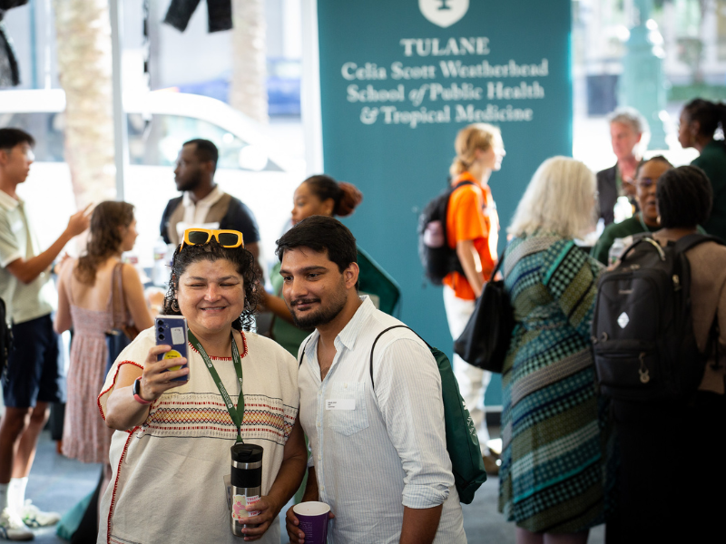 Two people smiling and taking a selfie at a busy school event.