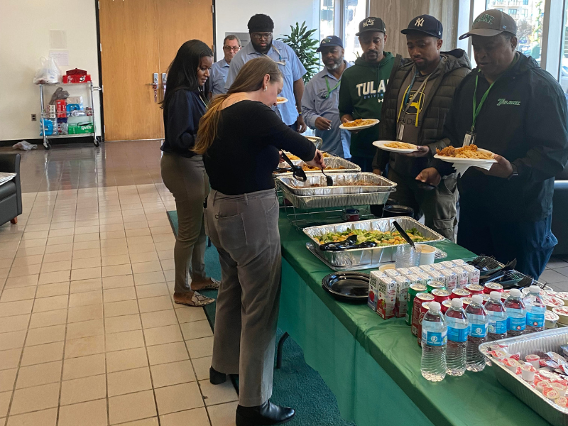 People serving themselves food from a buffet table at an indoor gathering.