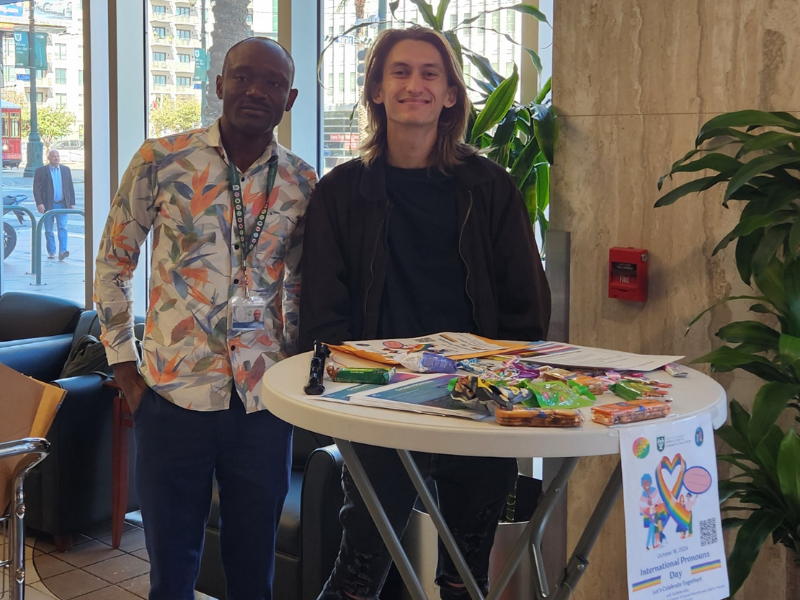 Two people standing behind a table with arts and crafts supplies in a bright indoor lobby.