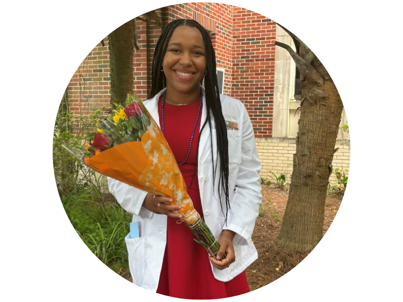 Amber Brooks, smiling, in white lab coat over red dress, holding a flower bouquet.