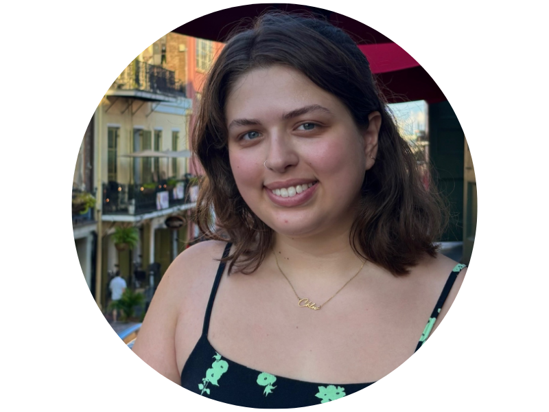 Chloe Garrett, smiling, wearing a sundress nad sitting on a balcony in a European town
