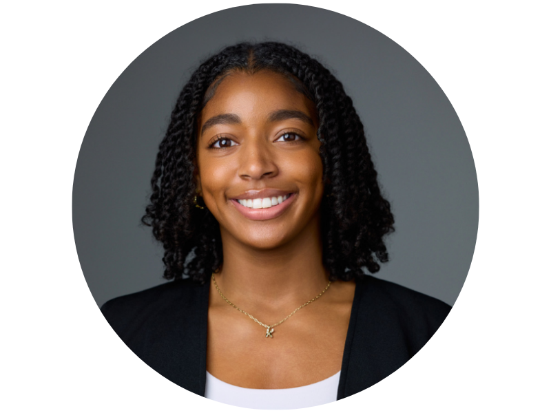 Kaia Todd, a smiling young Black woman with dark hair in a black blazer against a gray background.