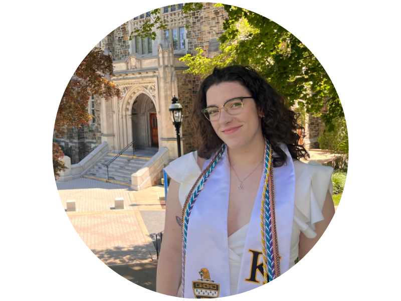 Smiling graduate, Kate Weiss, in white with a colorful stole in front of a stone building.