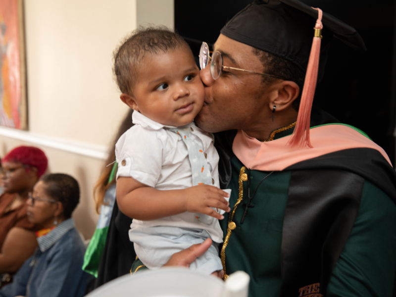 A graduate kissing their adorable child on the cheek