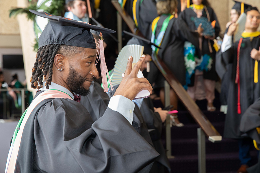 Happy graduate in cap and gown takes a selfie, making a peace sign.