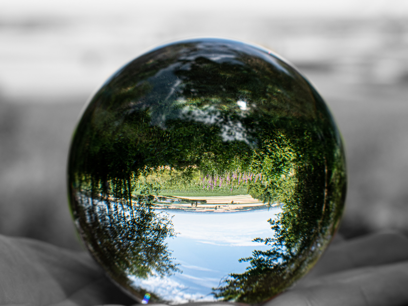 Glass sphere with inverted colorful lake and trees, against a grayscale background.