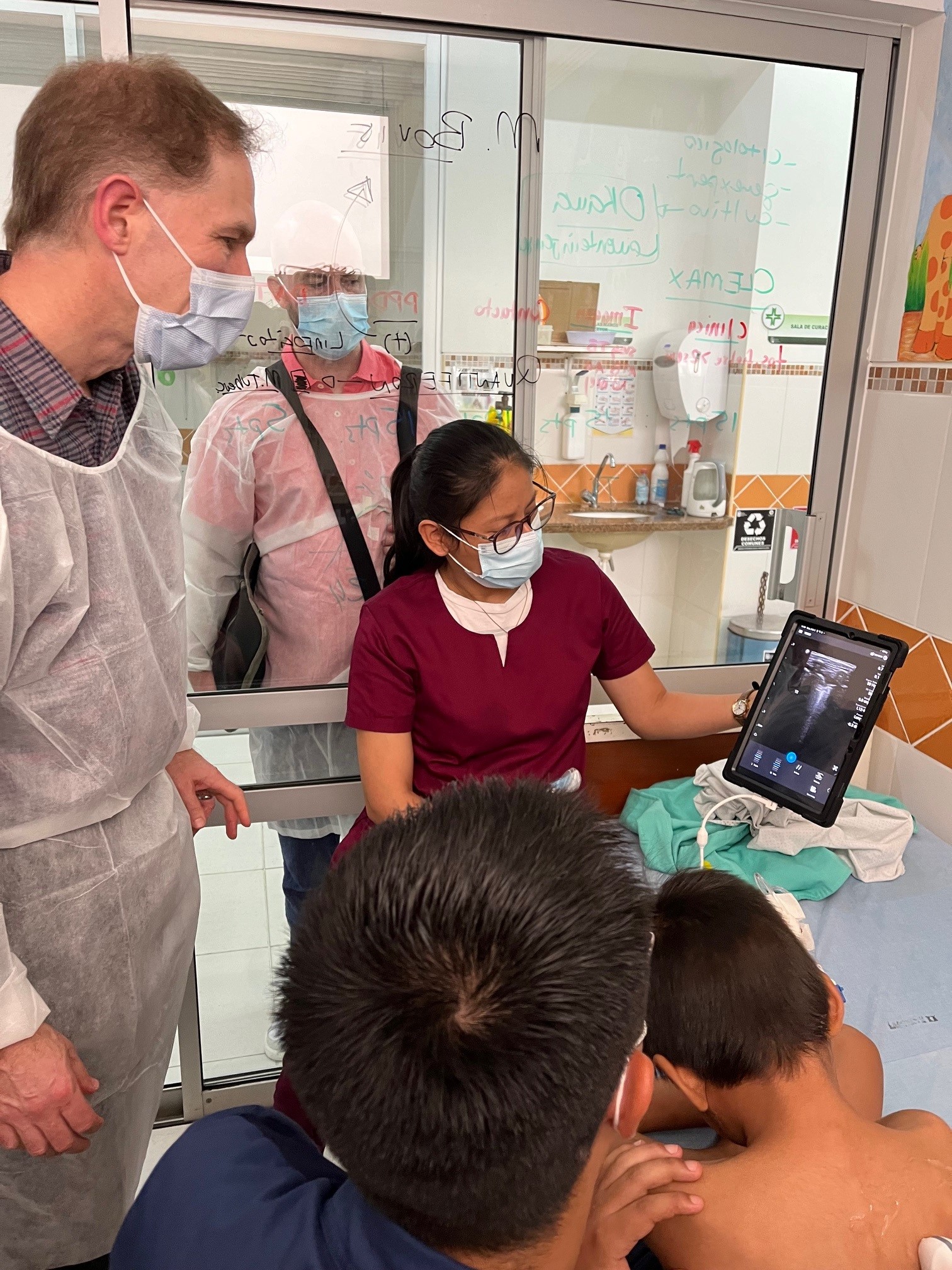 Medical professionals and children observing TB imaging on a tablet in a clinic.
