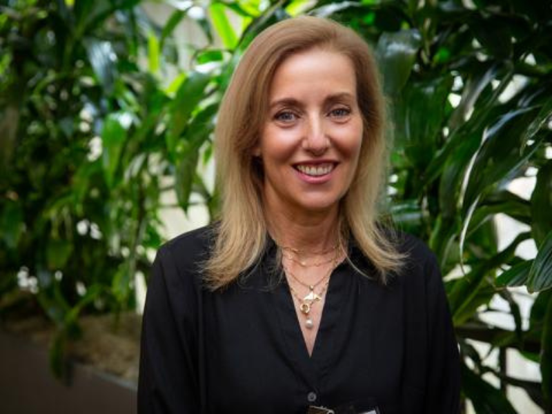 Felicia Rabito smiling in a black shirt against a green plant background.