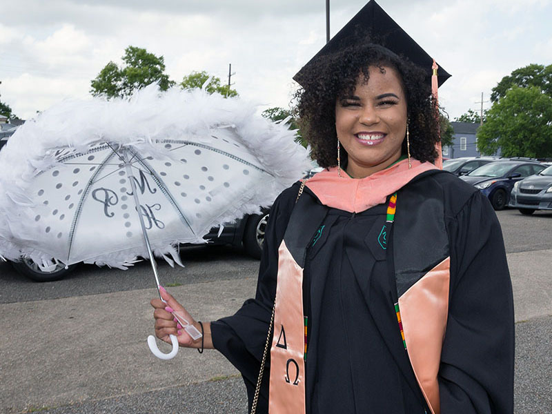 A recent graduate poses in her robes, stoles, and with a second line parasol