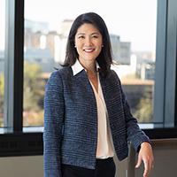 Paula Song, wearing a suit, smiling, and one arm resting on a window sill