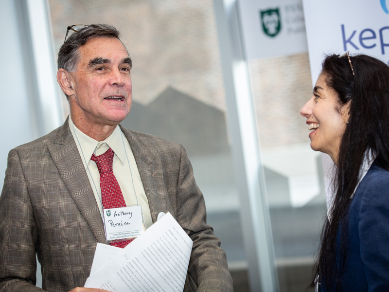 Man in suit and smiling woman in blue jacket talking at an event.