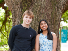Smiling young man and woman standing in front of a large tree trunk.
